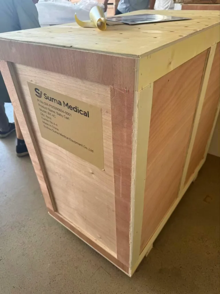 A wooden shipping crate from Suma Medical with product labeling including product details and company information, placed on a concrete floor.