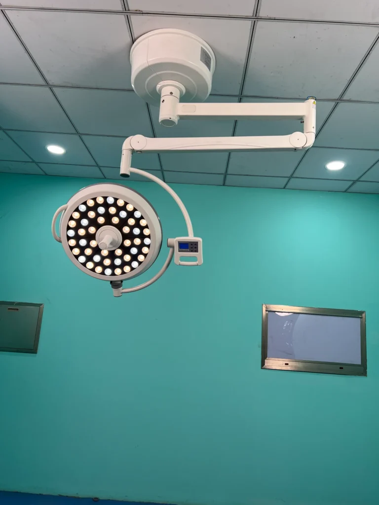 Ceiling-mounted surgical light with LED bulbs and adjustable arm installed in a sterile operating room with teal walls.