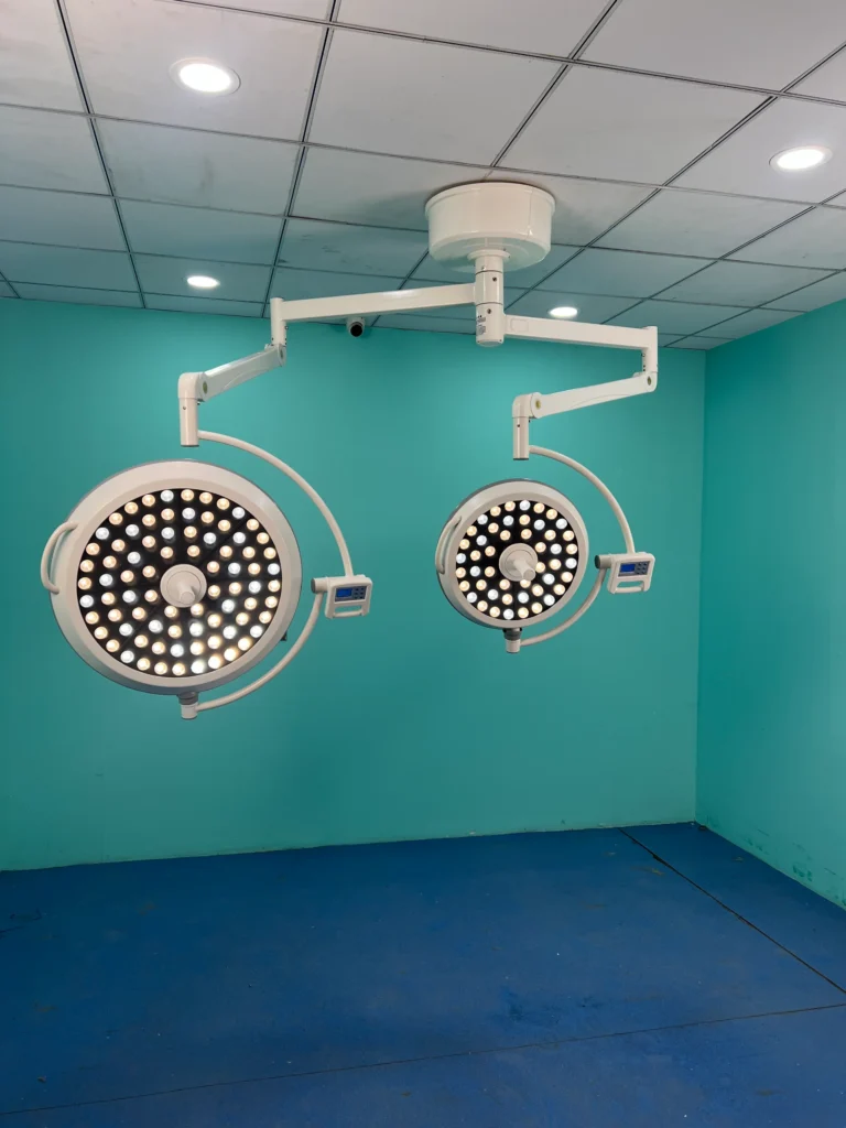 Ceiling-mounted surgical lights with LED technology in a teal-colored operating room. The lights are adjustable and provide bright illumination.
