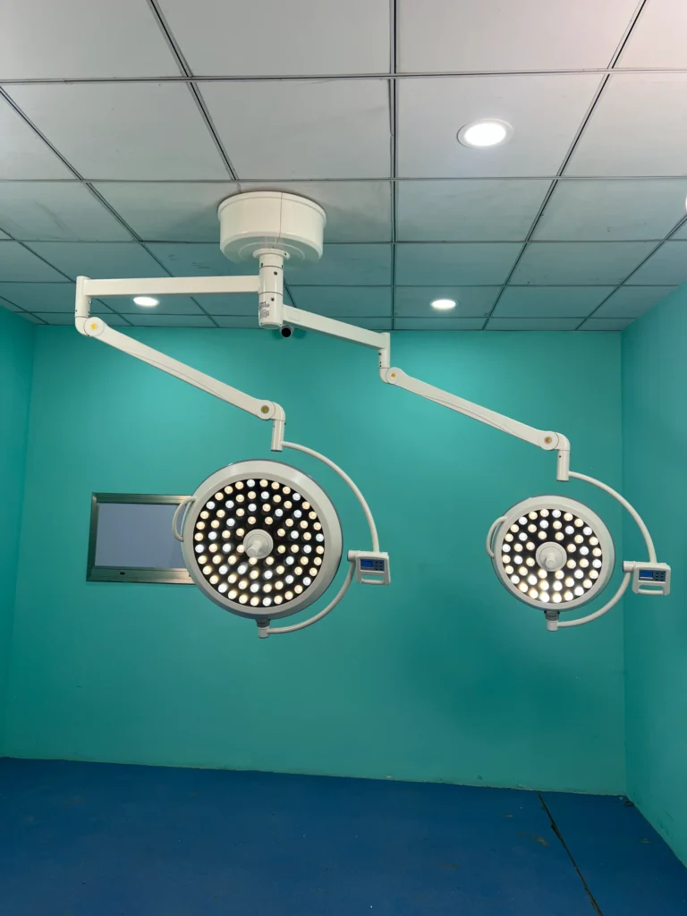 Two ceiling-mounted surgical lights with multiple LED bulbs in a teal-colored operating room with a tiled ceiling.