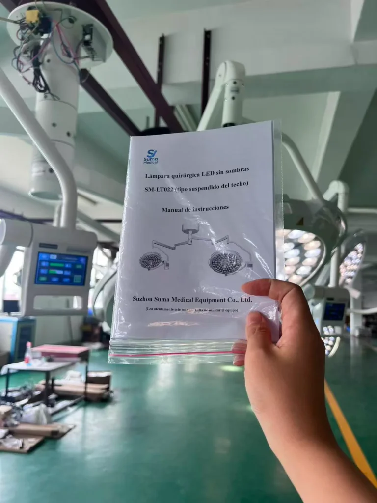 A hand holding the instruction manual for the SM-LT022 surgical LED lamp in a medical equipment facility. The background shows the lamp and related equipment.