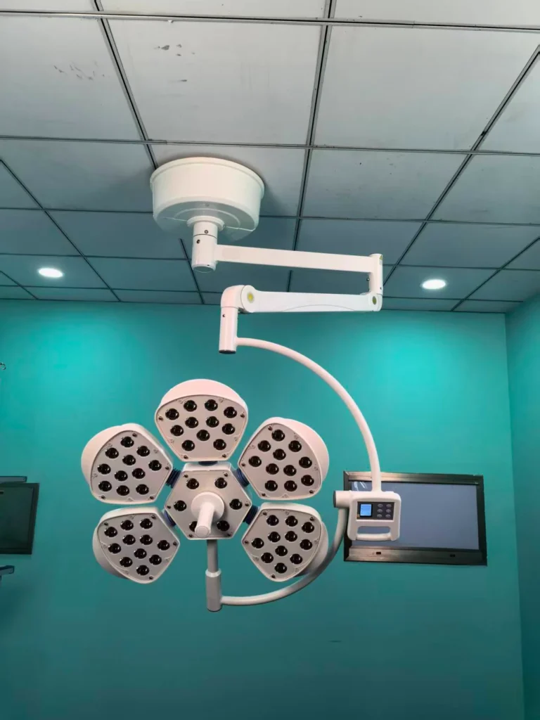 Ceiling-mounted surgical LED light with a petal-shaped design in a teal-colored operating room.