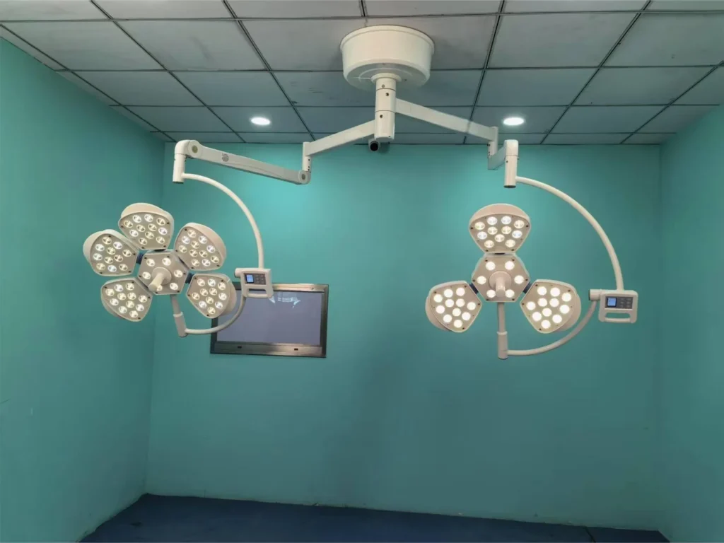 Ceiling-mounted surgical LED lights with adjustable arms and multiple light panels in a teal-colored operating room.