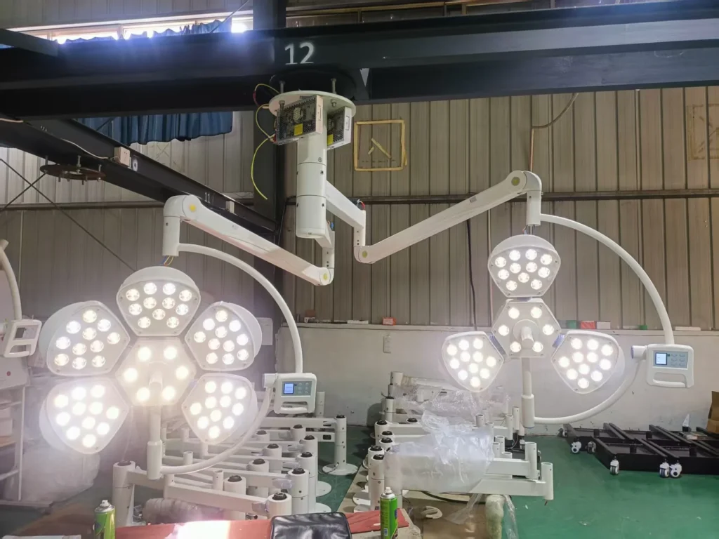 Two sets of modern LED surgical operating lights being assembled in a factory with metal beams and green floor.