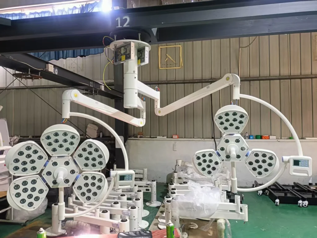 Surgical operating lights with multiple LED panels in an industrial setup, showing mechanical arms and assembly equipment.