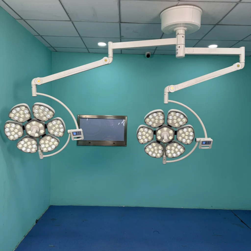 Two ceiling-mounted surgical operating lights with LED panels in a teal-colored medical room with a ceiling monitor.