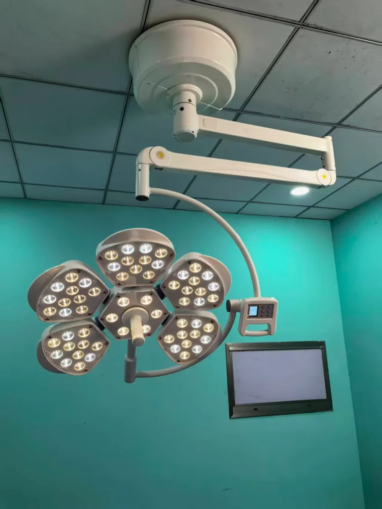 Overhead surgical operating room light with multiple LED panels and control panel in a medical facility.