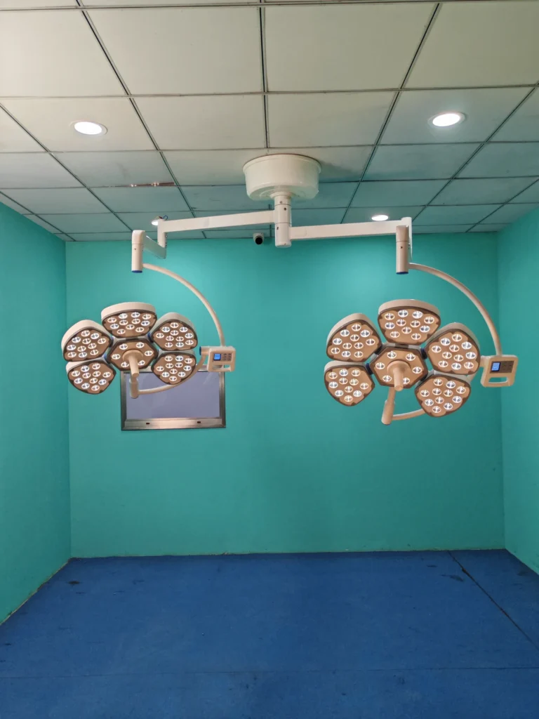 Ceiling-mounted surgical operating room lights with LED panels in a green-walled medical room with blue flooring.