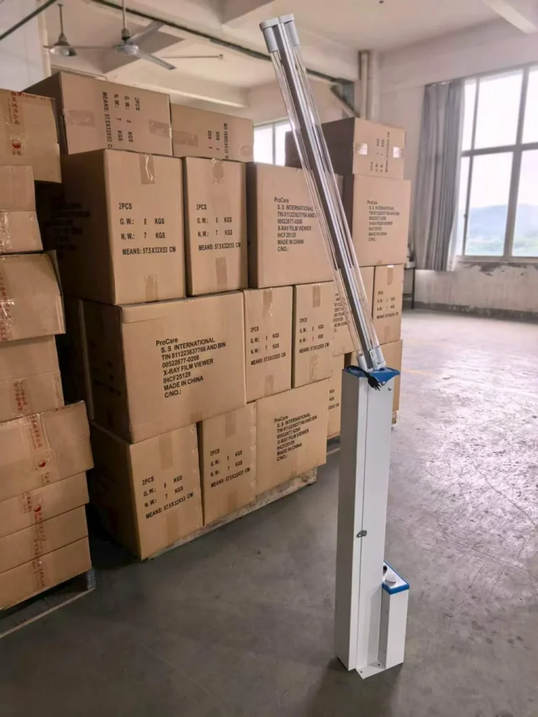 A UV sterilizer device in a warehouse surrounded by stacked cardboard boxes labeled with product information, next to a large window.