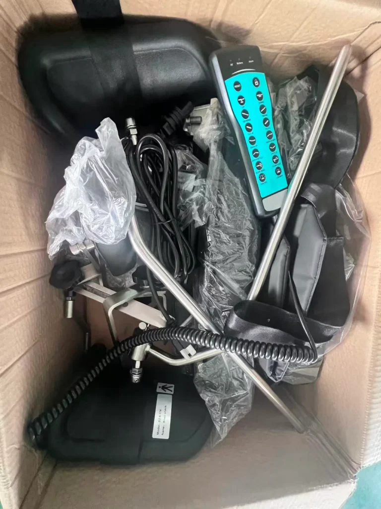 A collection of massage chair components including a remote control, cables, and metal rods organized in a cardboard box.