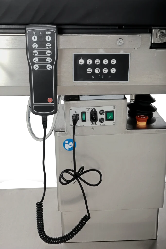 Close-up view of a medical examination bed's control panel and handheld remote, showing buttons, switches, and cords.