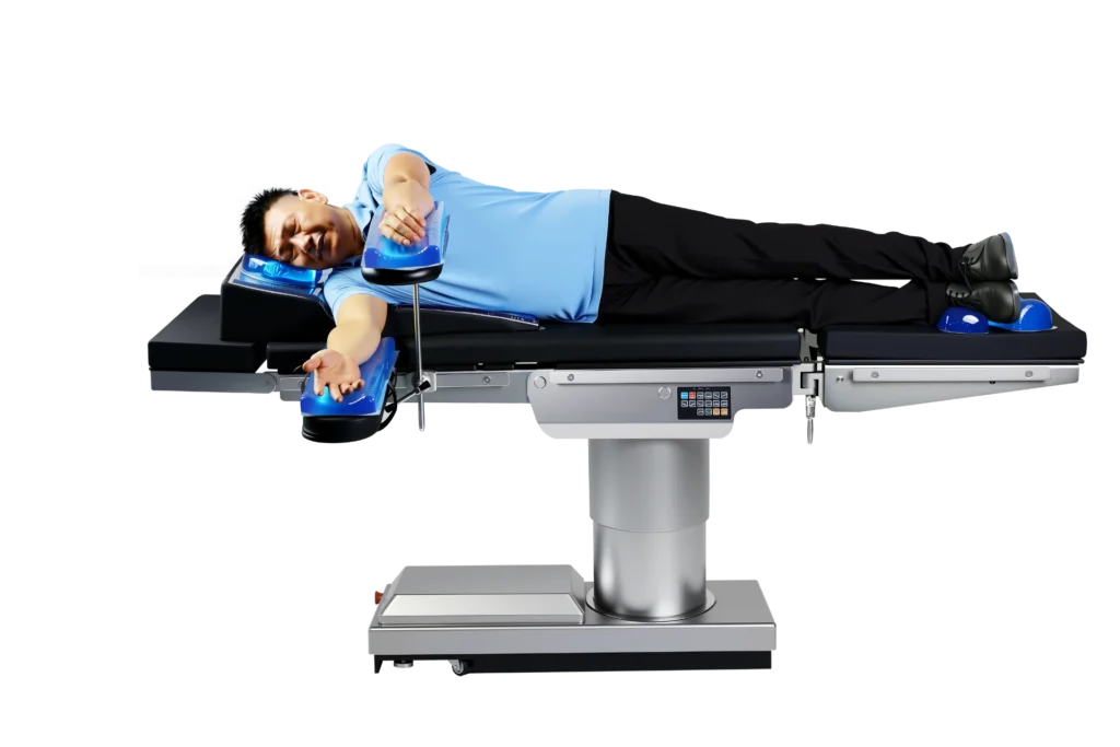 A patient lies on a modern medical operating table in a lateral position with positioning supports, wearing a light blue shirt and black pants.